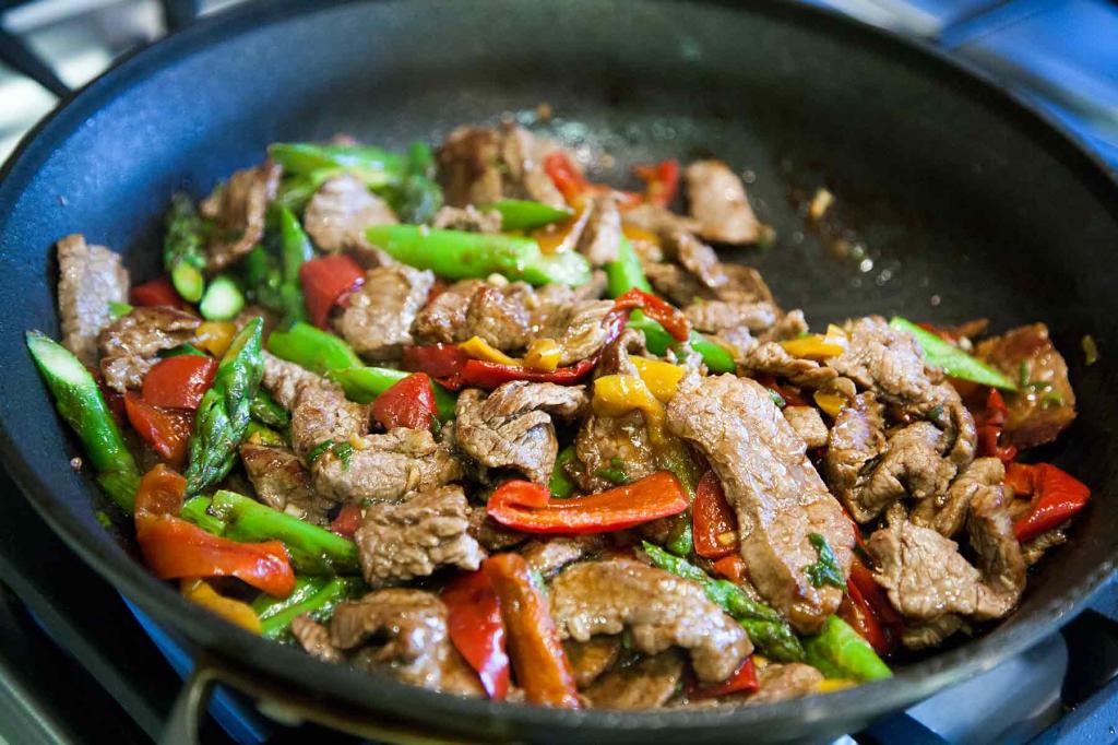 Meat in a wok recipes with vegetables Before you start cooking, select the meat. You can buy beef tenderloin or thin alternative steaks, such as Hanger steak or Skert. In the case of the last two, the meat is cut in strips across the fibers. Learn more about cooking alternative steaks by reading this article. We will cook meat with vegetables in a wok using a tenderloin. The tenderloin is a valuable part. It is dietetic and gentle in its structure. There are few fat streaks in it. Such a tasty piece of meat is a guarantee that your dish will be perfect. Beef in a wok pan is cooked very quickly, so we chop the meat in thin strips across the fibers, as for beef Stroganoff. Put the meat on a well-heated frying pan and immediately start stirring. The beef will cook for 10 minutes. Ginger, garlic and chili pepper, soy sauce and curry are traditionally used as spices. These are basic recommendations. In fact, the meat in the wok recipes are very diverse. We will prepare spicy meat with vegetables and corn cobs. We take the beef tenderloin, take it out of the refrigerator, let it heat up to room temperature, dry it and cut it into thin strips. Pre-cut all the vegetables. Onions and peeled sweet peppers are cut into large slices or half-rings. Carrots should be cut smaller. Corn cobs are cut in half, garlic cloves are cut in plates. Chop the green onions. In a preheated frying pan, fry the meat in small portions for 8-10 minutes, stirring constantly. After the meat, the vegetables are fried separately for 2-3 minutes. They are laid in order of hardness. That is, carrots before, and green onions at the very end. When the vegetables are almost ready, add the corn and sweet pepper, sesame seeds and sugar. Return the meat to the wok and prepare all the ingredients now. Tomato paste and soy sauce are added to the pan, and then the dish is salted and peppered to taste. Now the wok is not frying, but stewing and softening of all components. That's the whole recipe for cooking meat in a wok. Without taking into account the preparation, the main process takes about 20 minutes. The cooked meat with vegetables remains to be removed from the heat and spread on plates.Meat in a wok recipes with vegetables